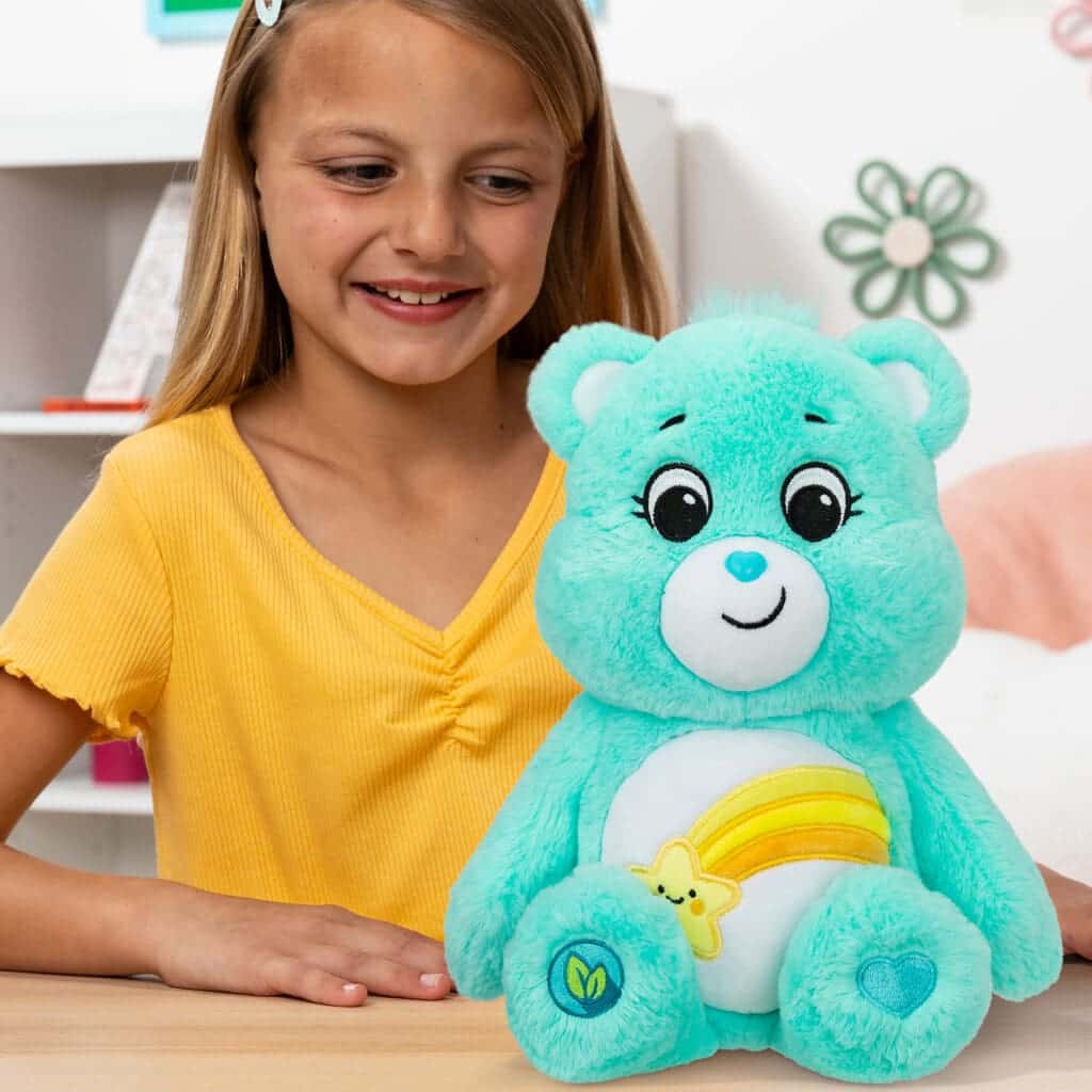 Light Blue Wish Bear on table with young girl smiling.