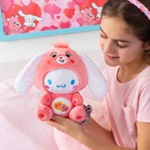 Young girl looking at Care Bears Funsize Cinnamoroll plush displayed in a lifestyle setting, featuring a cute and cuddly design with a pink heart emblem on its stomach, promoting love and friendship.